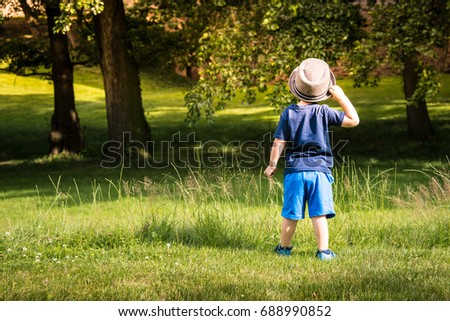 A little boy with dads hat amazed by beauty of a castle park greenery and trees. Serene nature in Prague city suburb - landscape background photo