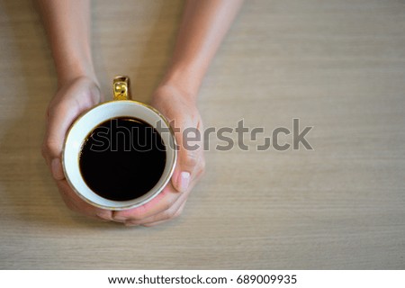 Female hands holding a cup of coffee with espresso coffee on wooden table, top view and copy space