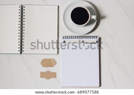 Scattered coffee beans and coffee espresso cup on marble backdrop. Notebook on marble