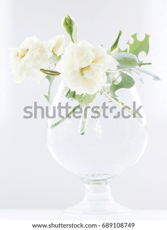 Three delicate blossoming white roses in a glass glass of water on a light background.