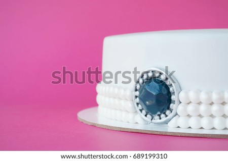 Cake baking with white mastic decorated with beads from pearls, jewelry of stone on pink background. Picture for a menu or a confectionery catalog. Close up.