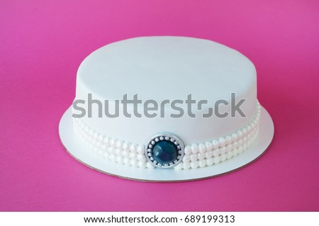 Cake baking with white mastic decorated with beads from pearls, jewelry of stone on pink background. Picture for a menu or a confectionery catalog.
