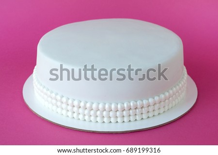 Cake baking with white mastic decorated with beads from pearls on pink background. Picture for a menu or a confectionery catalog.