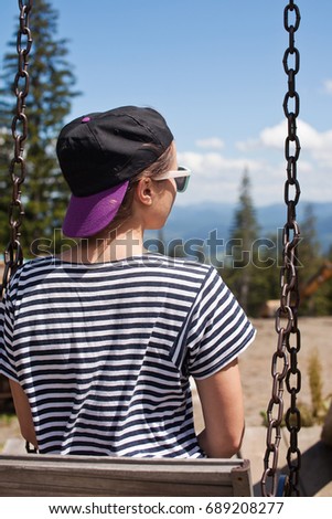 A young girl is riding on a swing overlooking the mountains.