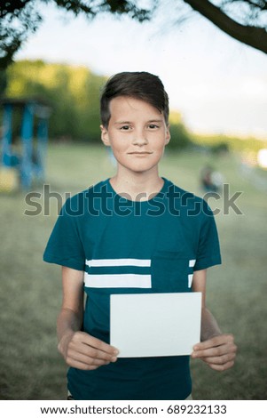 Smiling teenager with blank paper in his hand on nature in summer park. Advertising concept