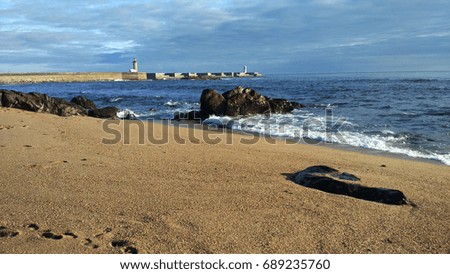Sand and stones on a beach, with a lighthouse in the background