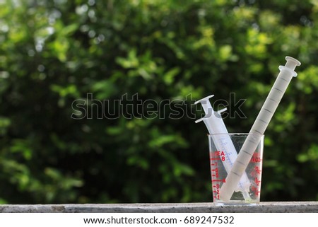 Ants eating medical syrup in unclean measuring cup and syringes after use for a baby with blurry green natural background and clear sunset light