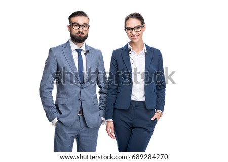 smiling businesswoman and serious businessman in suits standing and looking at camera, isolated on white 
