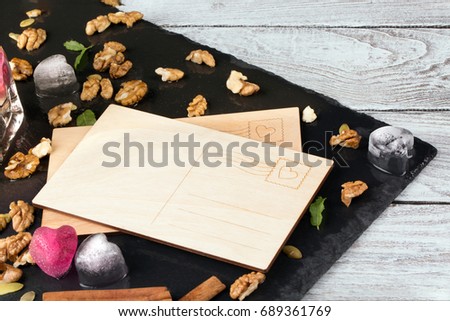 An empty postcard on a wooden background. Cute ice hearts, cinnamon, nuts and a note. Invitation, celebration concept. Copy space.