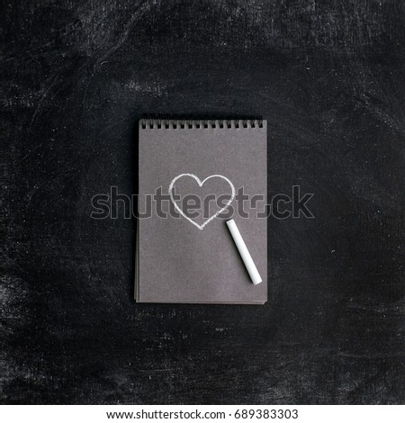 Chalk heart in a notebook on a black wooden background, the concept of a Valentine's day card. Flat lay, top view