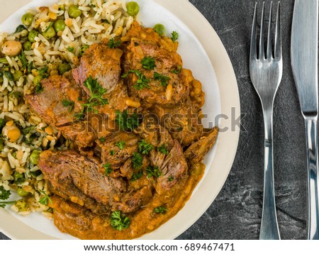 Aromatic Lamb Curry With Vegetable Rice Against a Black Slate Tile Background