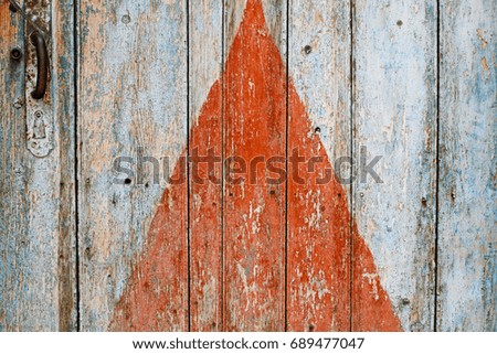 Painted red triangle on the old wooden door with handle as background or texture