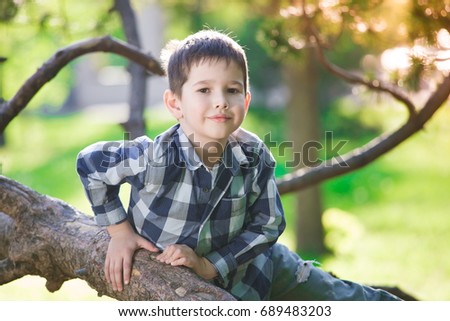 Beautiful little brunet hair boy, has fun smile face, happy eyes, dressed in blue plaid shirt, play in tree. Kids portrait. Creative concept. Summer time. 