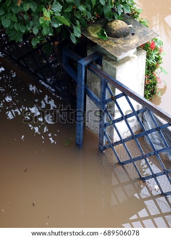 global warming effect in town, high level flood water in urban zone authentic picture shows brown dirty water level at blue painted iron metal house fence  