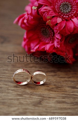 Gold wedding rings and red gerbera lie on wooden table