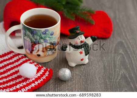 Tea in the year of the dog. A mug of tea with a picture of a dog in Santa Claus hat for the new year. Red knitted scarf, snowman and tea with the image of a dog create coziness and a New Year's mood.