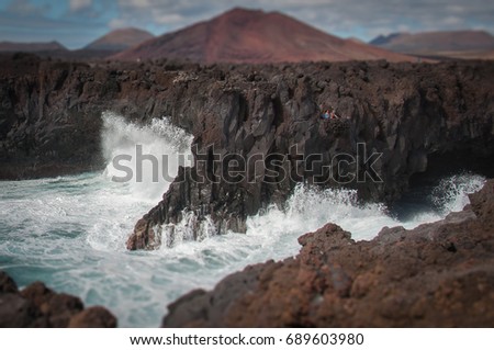 Tilt shift effect of people watching big fringing waves on rocky coastline, Los Hervideros, Lanzarote, Canary Islands
