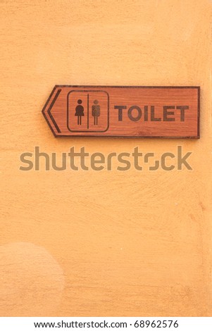 Toilet wood label on orange wall.