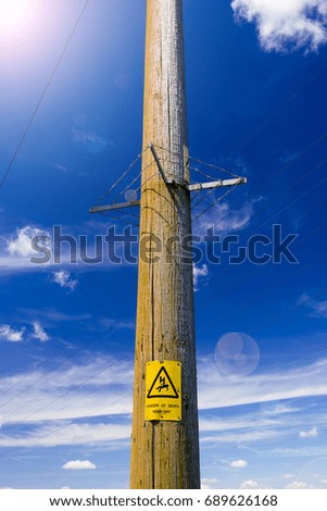 Electricity poles reach up into the deep blue sky. A warning sign warns of impending danger