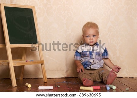 Adorable little boy sitting near drawing board. Cute toddler among chalk for drawing and looking at camera.