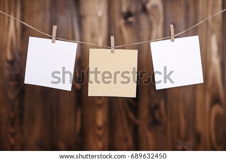 Close up of three white note papers hung by wooden clothes pegs on a brown wooden background