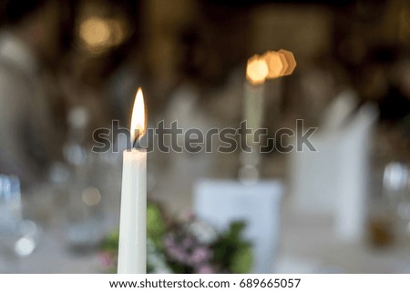 Closeup of burning white candle romantic dinner table memory memorial in front of bokeeh background