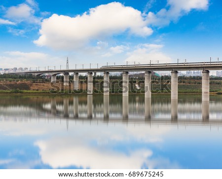 Low Angle View Of High Speed Train On Bridge Over River against cloudy sky.