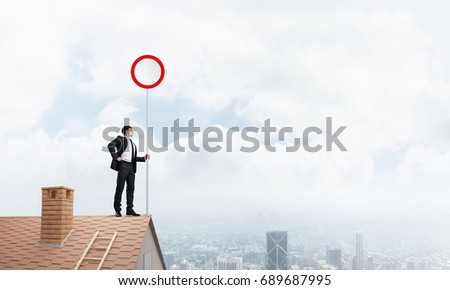 Businessman standing on house roof and holding stop sign. Mixed media