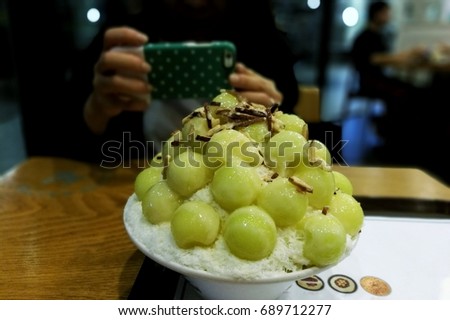 women taking photo of sweet melon bingsu dessert with smart phone.