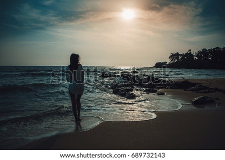 Silhouette of a young woman standing on the sand at the beach in the evening, soft focus.