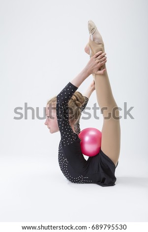Sport Concepts. Caucasian Female Rhythmic Gymnast In Professional Competitive Black Sparkling Suit Doing Backbend Stretching Exercise With Ball in Studio On White. Vertical Image Composition
