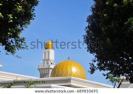 Islamic mosque building with yellow dome and minaret with blue background