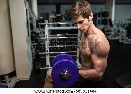 Side view of confident young handsome man in sportswear exercising with dumbbell at gym