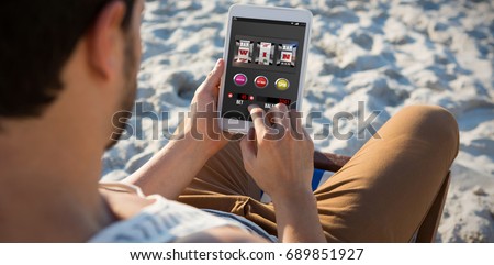 Slot machine with text and numbers on mobile screen against high angle view of man using digital tablet at beach