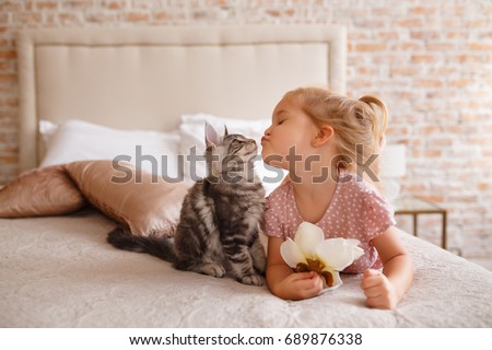 Little girl relaxing on the bed with her kitten. Child is kissing a cat Royalty-Free Stock Photo #689876338