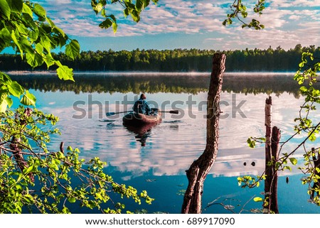 Morning summer lake landscape with plants reflections on water surface and boat with fisherman