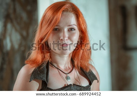 Red-haired young goth girl in an abandoned building against the backdrop of ruined walls and sunlight