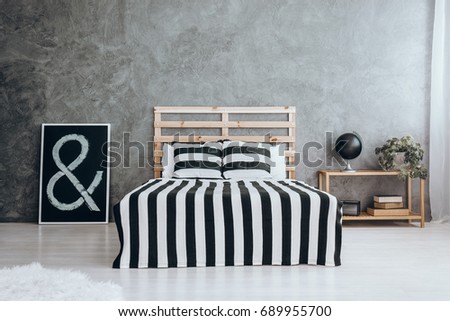 Black picture on the white glossy floor next to king-size bed with stripped coverlet