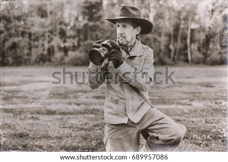 Old sepia photo of explorer with hat in the field holding camera. 