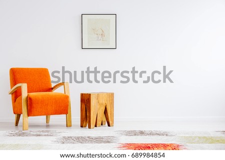 Trendy orange chair next to creative coffee table with bright picture above