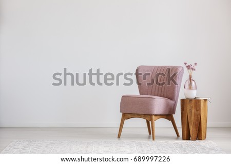 Cute pink flowers in glass vase placed on wooden table standing by small chair Royalty-Free Stock Photo #689997226