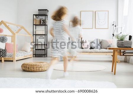 Blurred view of energetic young girl in dress running in trendy room with plush pillows