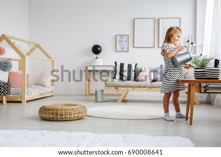 Young smiling blonde girl watering plants with watering can in cute pastel scandi room