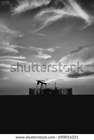 Silhouette of crude oil pump in the oilfield at sunset blue hour - Black and white edit