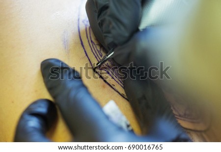 A professional tattoo artist introduces black ink into the skin using a needle from a tattoo machine. tattoo art on body.Makes a tattoo.Professional tattooist working tattooing in studio