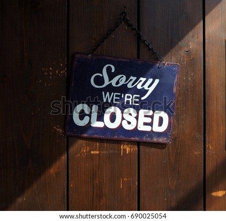 Sorry we are closed, blue and white retro sign on old wooden door with a shadow that divides it into a clear and dark part.