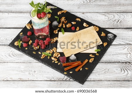 A beautiful composition of lovely postcards and colorful cocktail on a light gray background. Many berries, walnuts, cinnamon sticks and green leaves near the invitation cards.