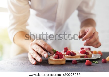 Preparation of cakes with raspberries on a table Royalty-Free Stock Photo #690075232
