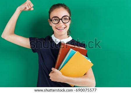 Smiling student hugging books and showing her biceps. Photo of teen near blackboard, education concept