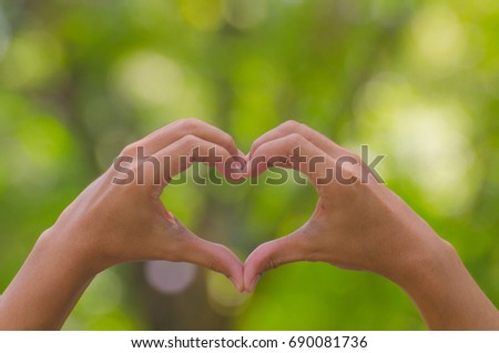 Hands with heart sign on green blur at garden background. Royalty-Free Stock Photo #690081736